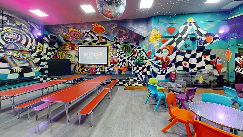 The seating area: long tables and benches in front of the screen, with the Wonderland murals