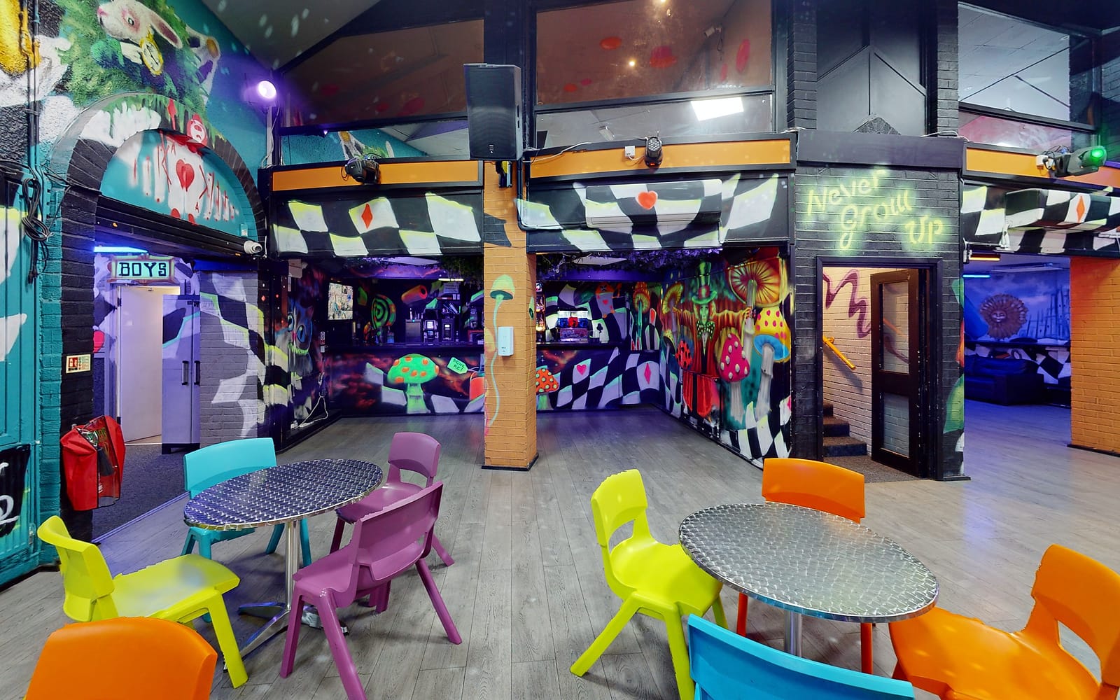 Tables and bright chairs in the main hall, under the Wonderland murals